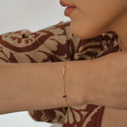 14k Gold bracelet with a red gemstone on a woman model's wrist, wearing a patterned garment.